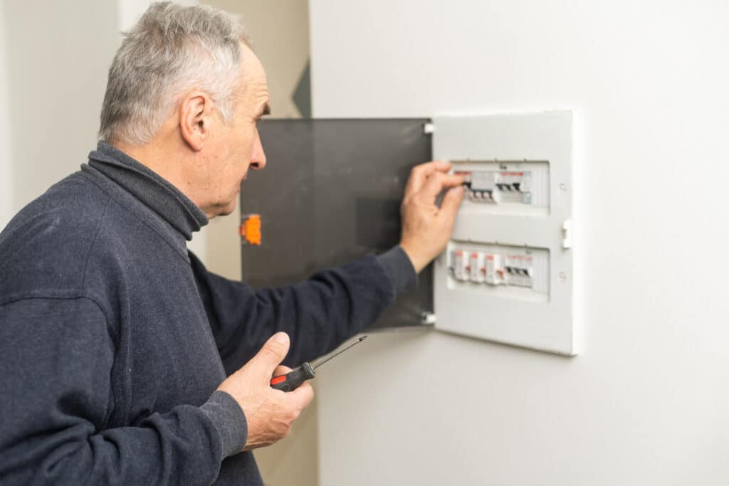 Mature man an electrician turning on circuit breaker in panel